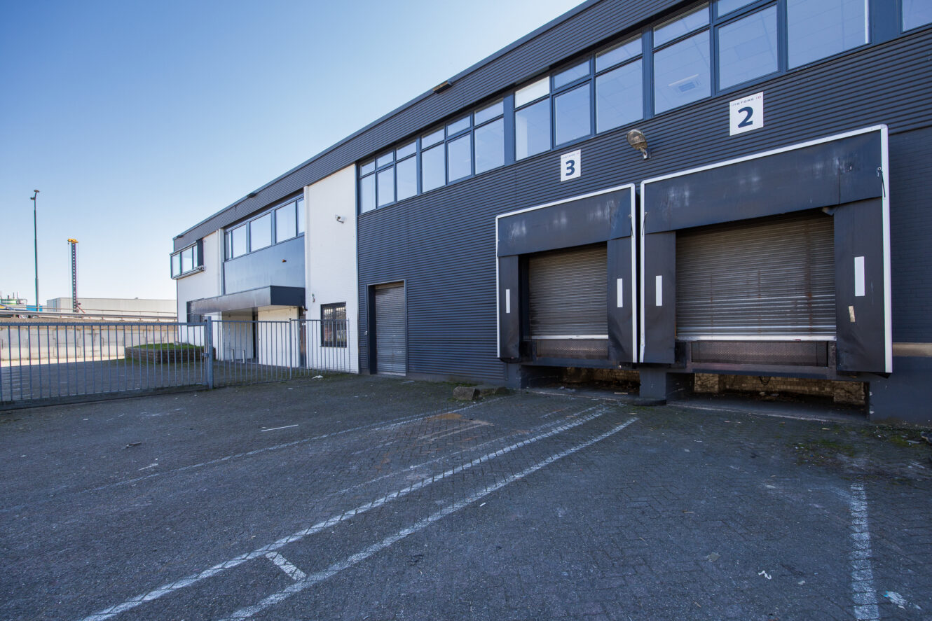 Een commercieel laadperron met twee gesloten laadperrondeuren met het label 2 en 3, grenzend aan een modern industrieel gebouw onder een heldere hemel.