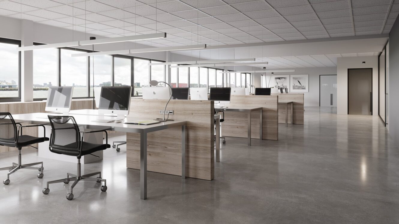 Modern open kantoor met rijen houten bureaus, zwarte stoelen, desktopcomputers, grote ramen en gepolijste betonnen vloeren. De ruimte is schoon en georganiseerd.