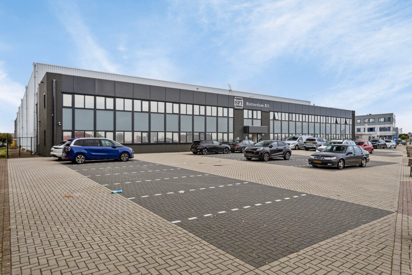 Een modern industrieel gebouw met grote ramen, met het label SFT Beheerburen B.V., en een aantal auto's geparkeerd op een verharde parkeerplaats onder een gedeeltelijk bewolkte hemel.