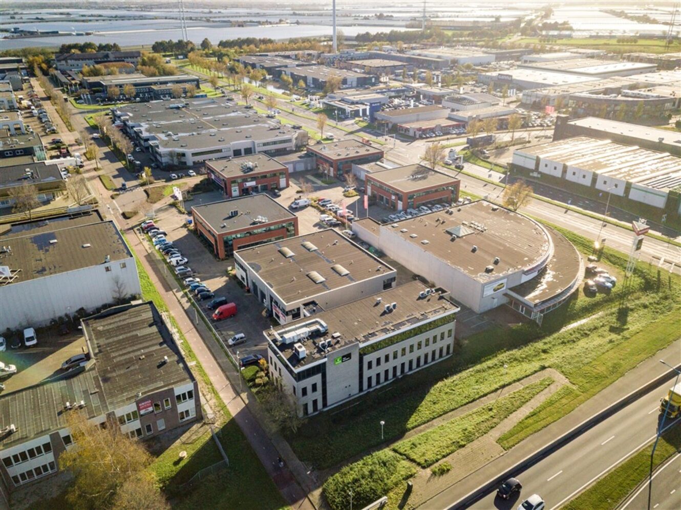 Luchtfoto van een industrieterrein met meerdere kantoor- en magazijngebouwen, buiten geparkeerde auto's, wegen en groenvoorzieningen.