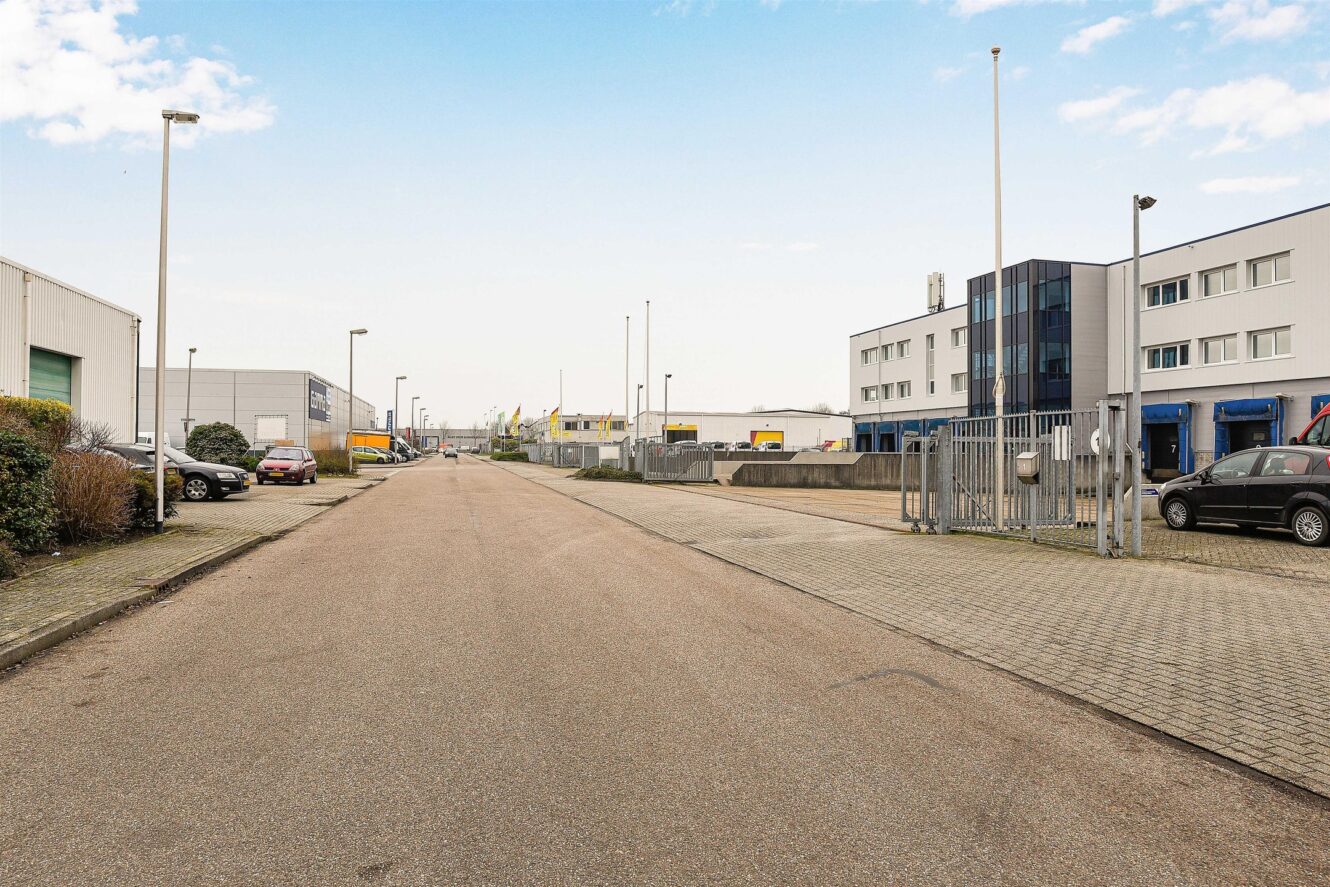 Lege industriestraat met geparkeerde auto's, moderne pakhuizen aan beide kanten en een heldere hemel boven je hoofd.