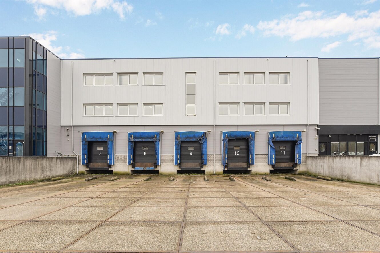 Een rij van vijf blauwe industriële laad- en losdeuren genummerd 7 tot en met 11 op een modern magazijngebouw met een betonnen kavel ervoor.