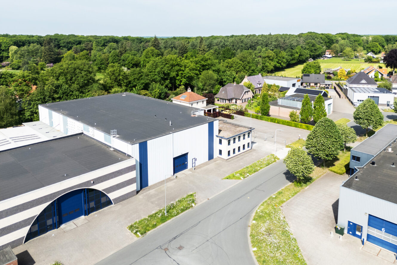 Luchtfoto van een industrieel gebied met grote magazijnen, kantoorgebouwen en nabijgelegen woonhuizen omgeven door groen.