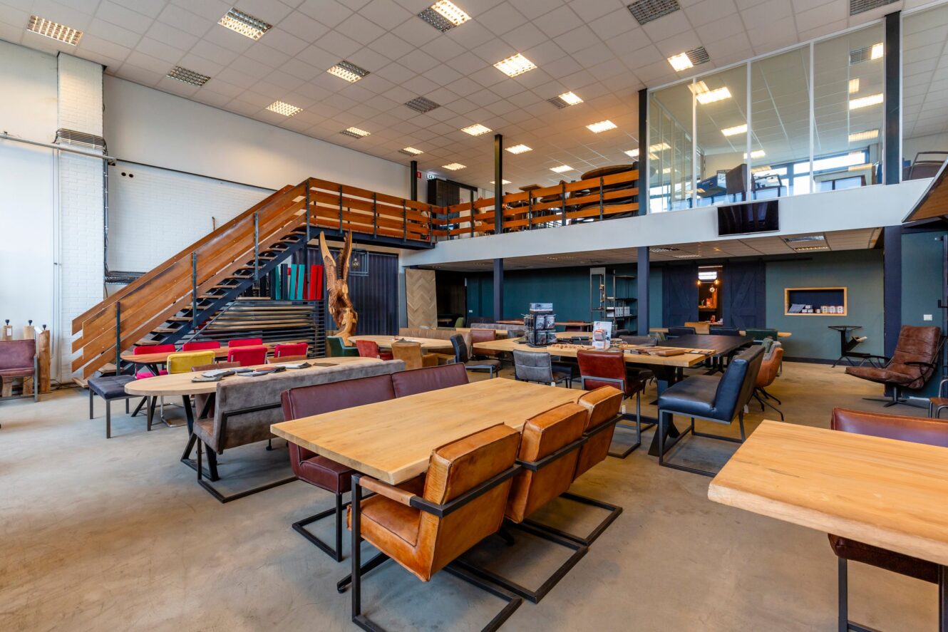 Ruim modern kantoor met houten tafels, leren stoelen, open trappenhuis en een tussenverdieping met vergaderruimten met glazen wanden.