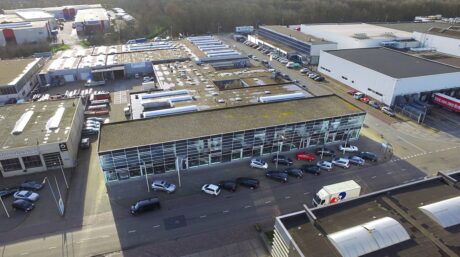 Luchtfoto van een industriegebied met magazijnen, geparkeerde auto's langs de straat en een gebouw met glazen gevel op de voorgrond.
