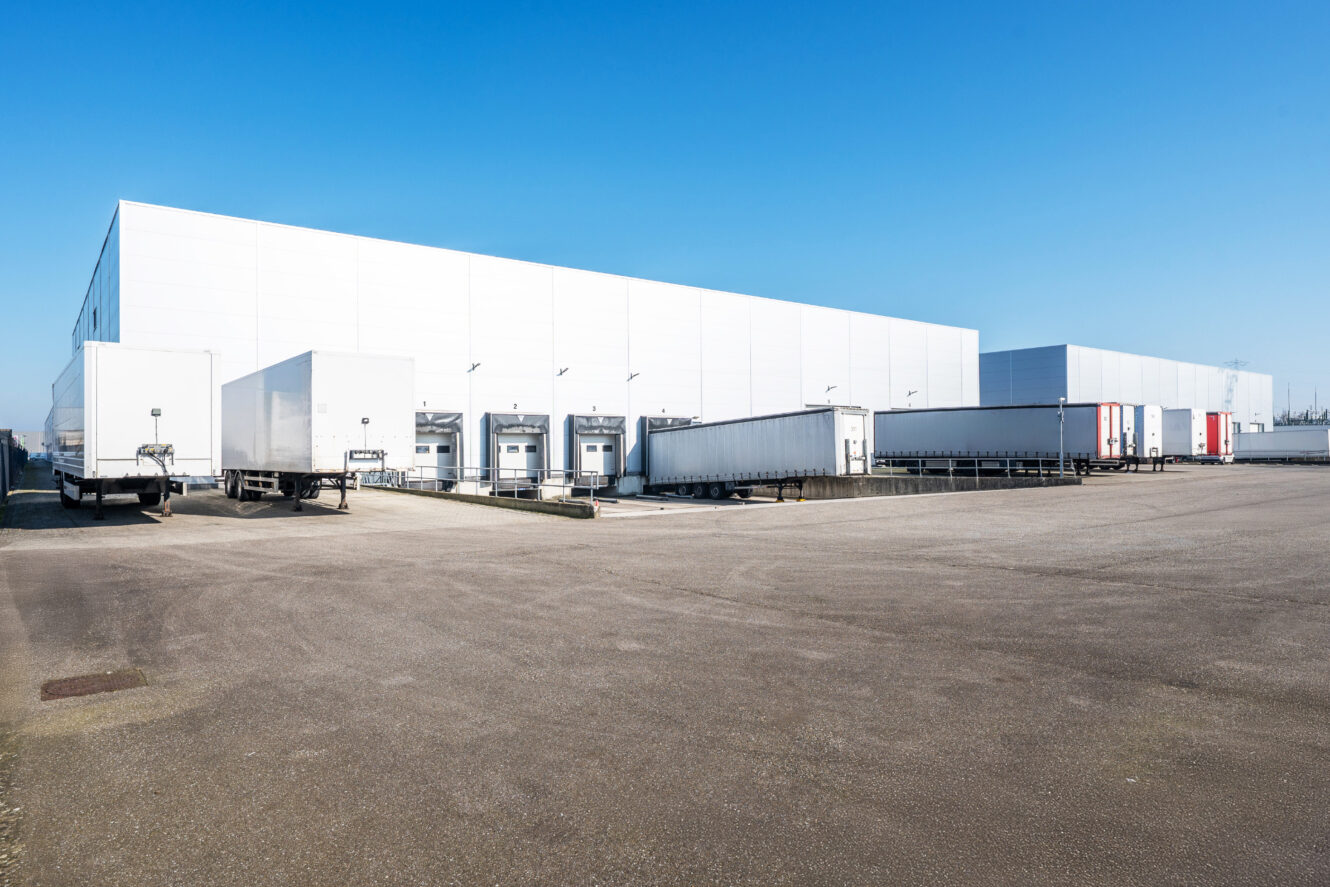 Groot magazijn met meerdere laaddocks en meerdere opleggers buiten geparkeerd op een heldere, zonnige dag.