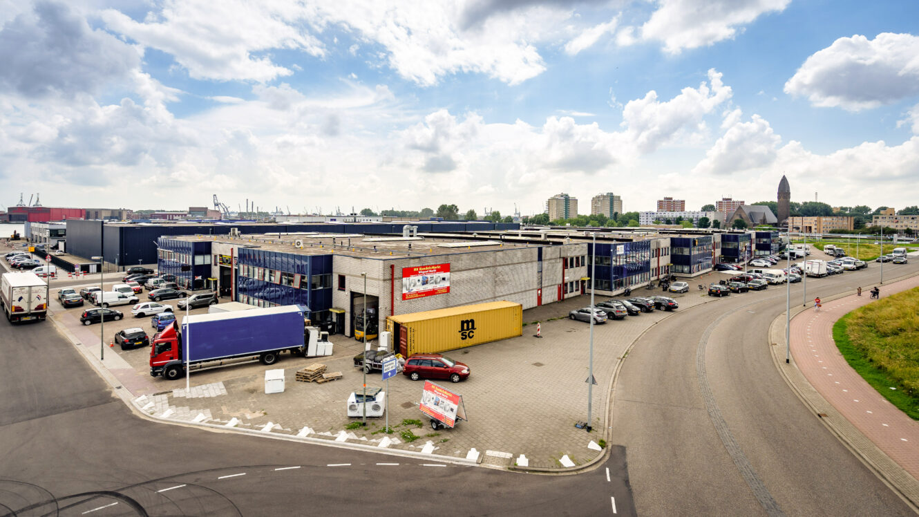 Industrieel magazijncomplex met meerdere vrachtwagens buiten geparkeerd, zeecontainers en kantoorgebouwen onder een gedeeltelijk bewolkte hemel.
