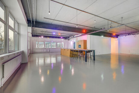 Ruime moderne kamer met hoog plafond, balkenplafond, hanglampen, grote ramen, glanzende vloer, kookeiland en barkrukken.