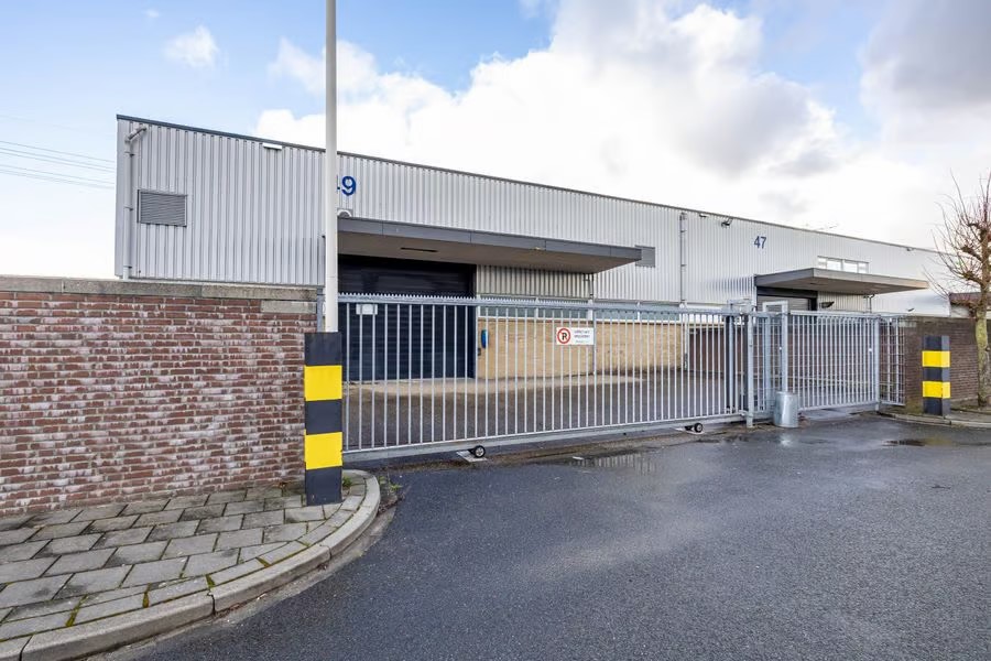 Een omheind industrieel pakhuis met genummerde laadperrons, bakstenen muren en nat asfalt aan de voorkant onder een bewolkte hemel.
