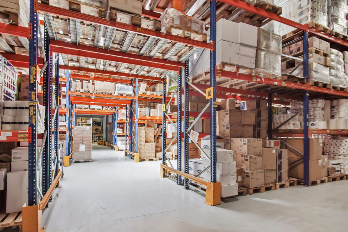 Lagerindretning med høje metalhylder fyldt med forskellige kasser og pakker, der skaber organiserede gange til opbevaring og adgang.
