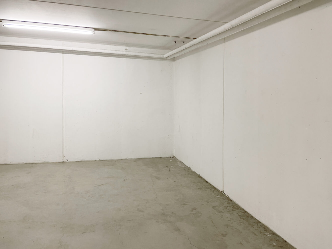 Et tomt, umøbleret rum med almindelige hvide vægge, et bart betongulv og et lysstofrør i loftet.