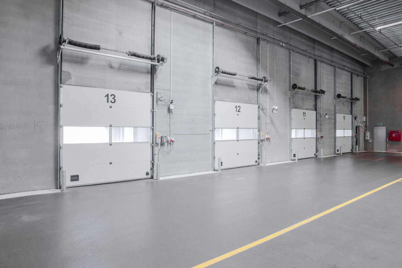 Fire nummererede læsseramper i et industrilager, mærket 13 til 10, med et gråt betongulv og -vægge.