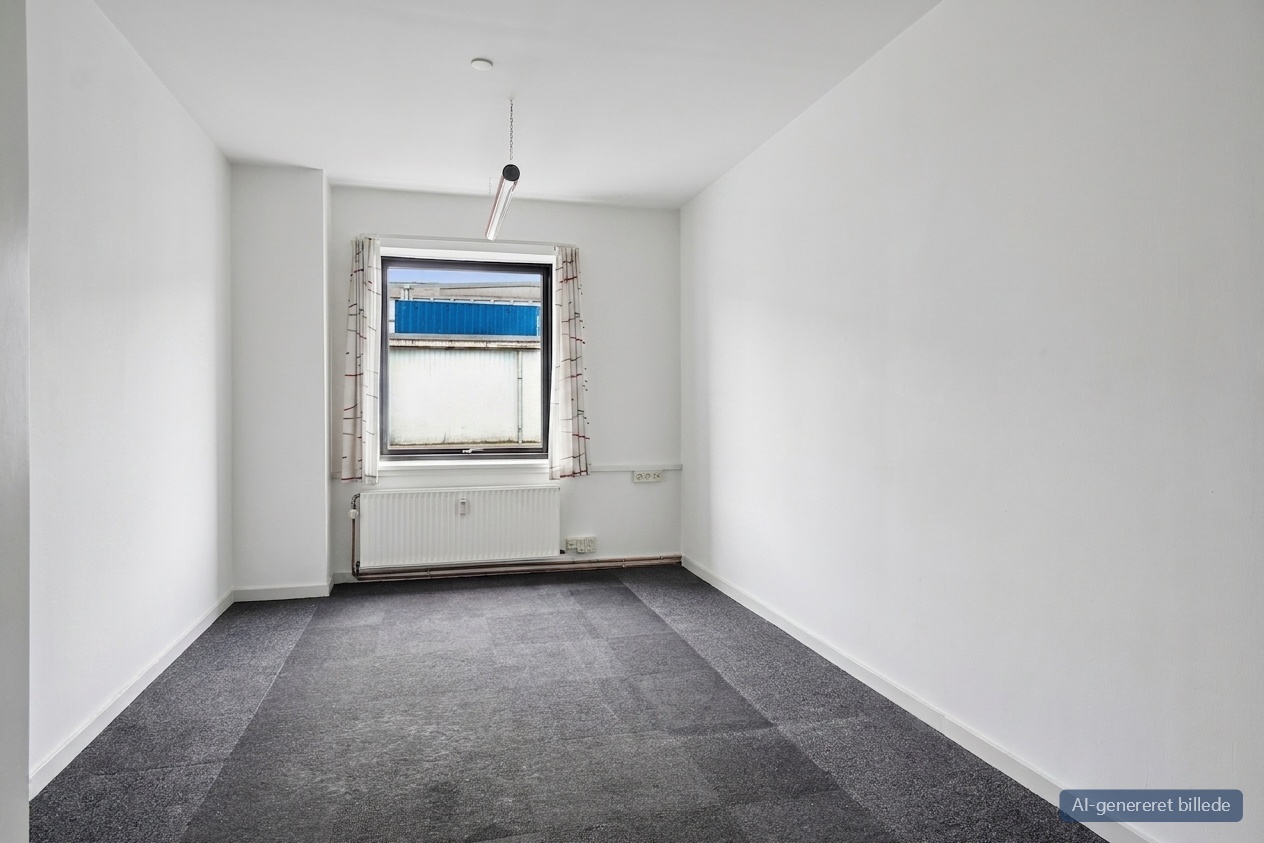 Et lille, tomt rum med hvide vægge, grå tæppefliser, et vindue med gardiner, en radiator nedenunder og en enkelt loftslampe.