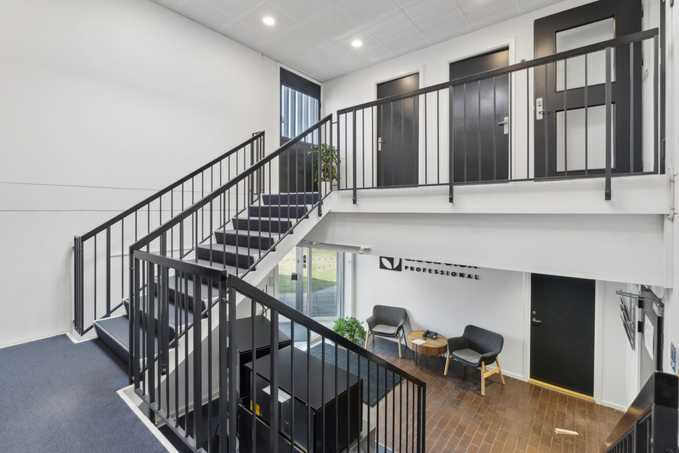 Moderne kontorindretning med en trappe, to stole og et lille bord nær indgangen og et rækværk med udsigt over det nederste niveau.