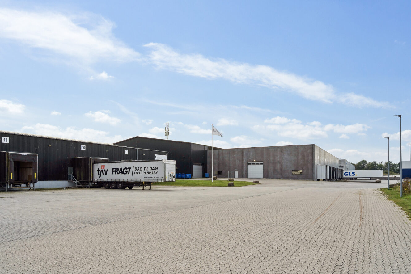 Industrielt lagerkompleks med læsseramper, trailere fra tjw FRAGT og GLS og en asfalteret gårdsplads under en delvis overskyet himmel.