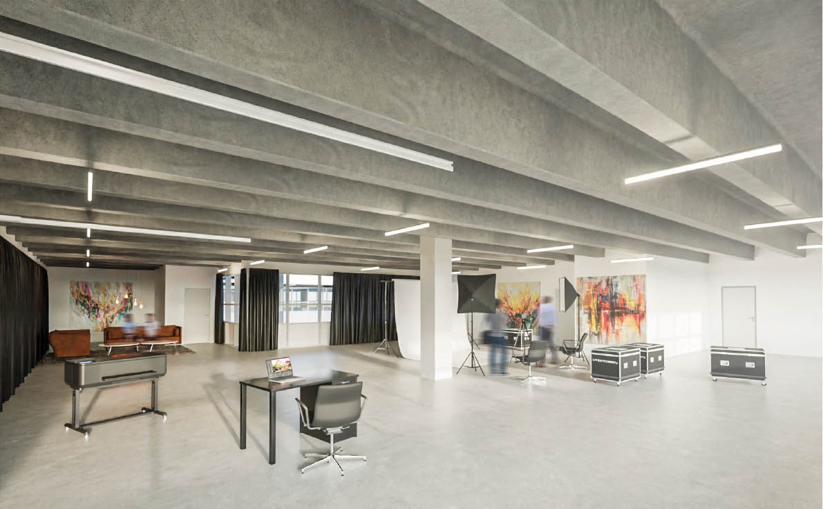 Rummeligt, moderne fotostudie med skriveborde, lysudstyr, store vinduer og farverige abstrakte malerier på væggene.