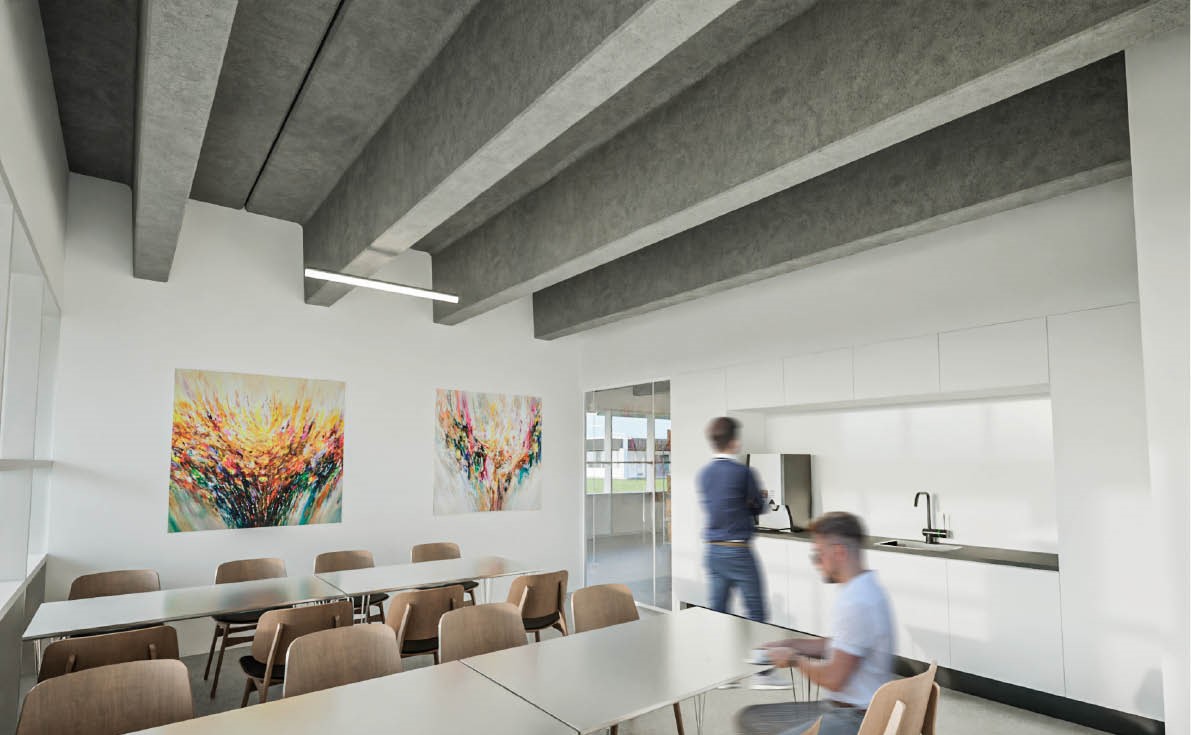 Et moderne pauserum med hvide vægge, borde og stole, abstrakt kunst på væggen, et tekøkken og to personer; en stående og en siddende.