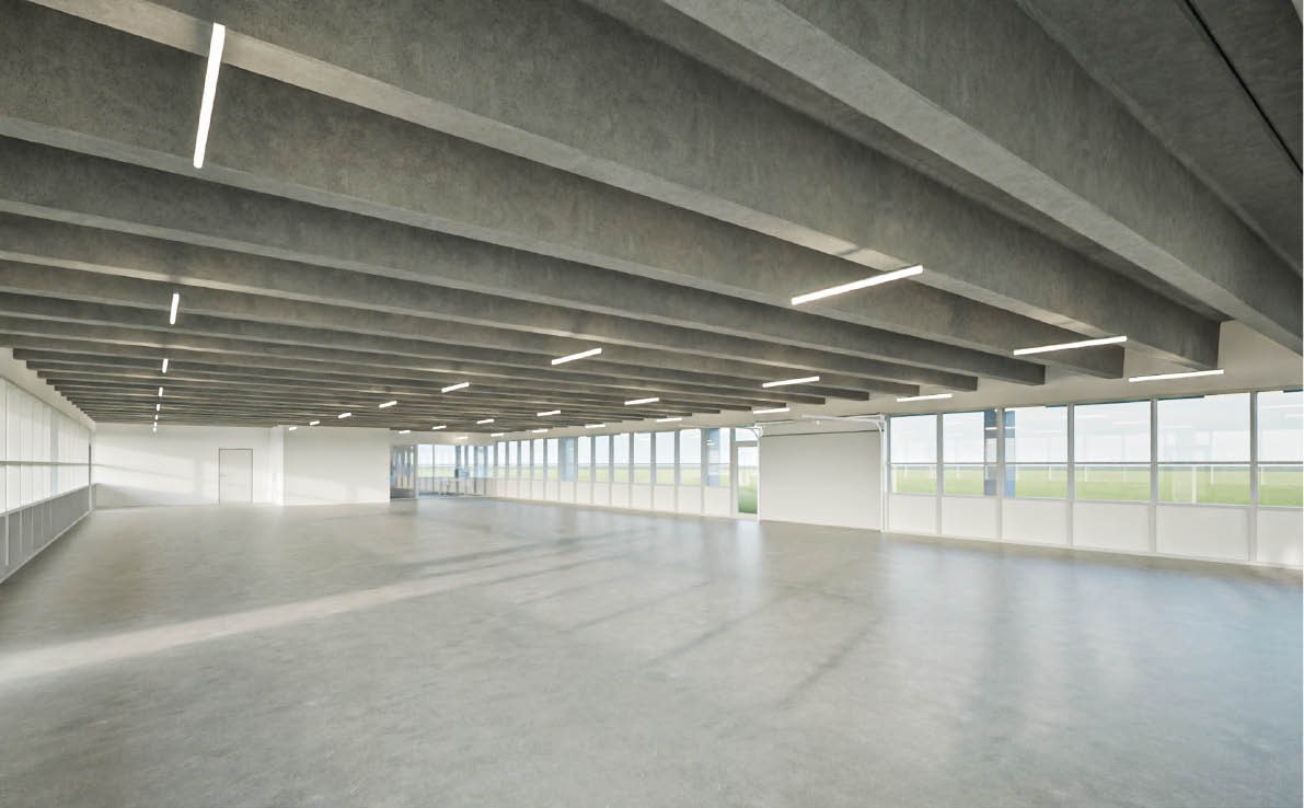 Stort, tomt rum med betongulv og fritlagt bjælkeloft, med lange vinduer langs den ene væg og lys, jævn overbelysning.