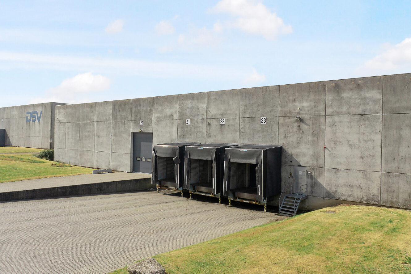 Tre læsseramper indbygget i en betonvæg, med lukkede porte og ramper, placeret på et asfalteret område med græsklædte omgivelser under en stort set klar himmel.