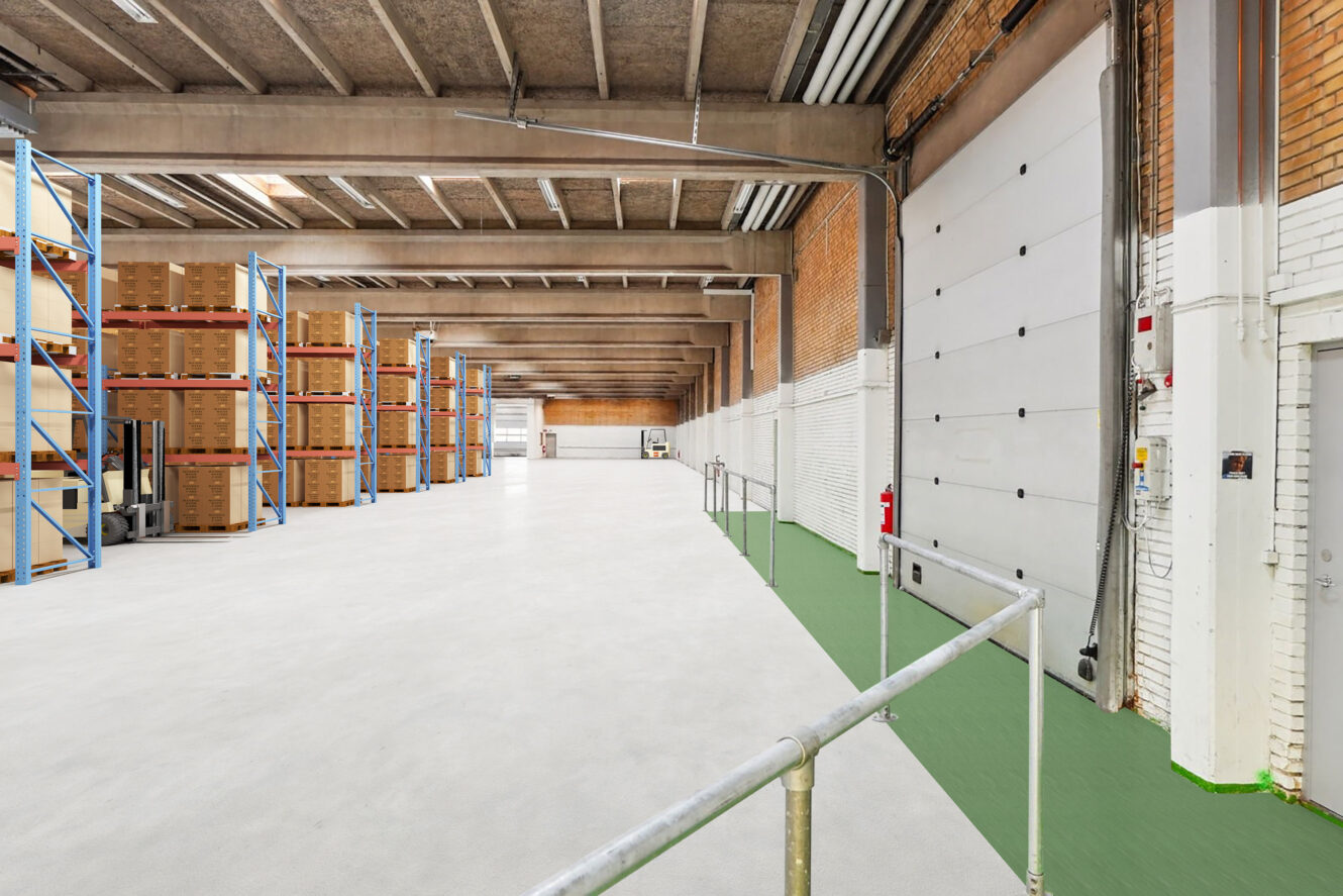 Rummelig lagerbygning med stablede paller på hylder, betongulv, højt til loftet og en stor rulleport til højre.