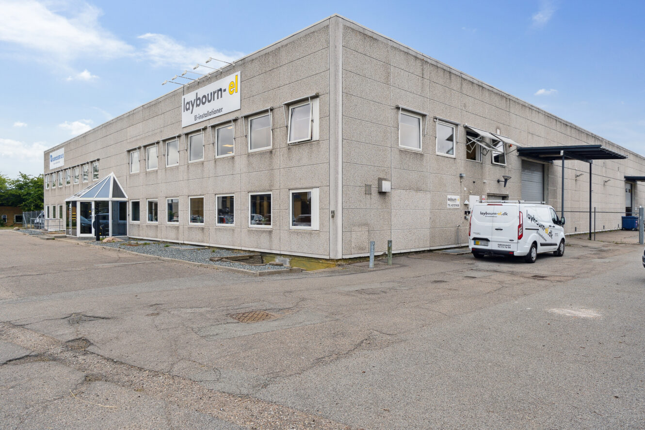 En toetagers industribygning med store vinduer og et skilt med teksten laybourn el. En hvid firmabil er parkeret udenfor på en stort set tom plads.