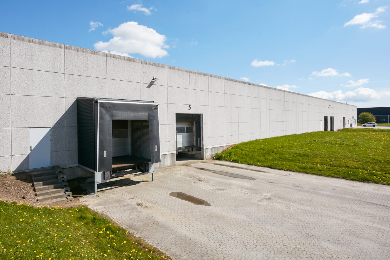 En læsserampe med to forhøjede båse, der er knyttet til en stor, hvid industriel lagerbygning på en solrig dag.