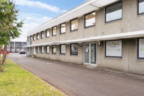 Kontorbygning i to etager med store vinduer og en glasindgang mærket 4; skilte for Global Hegn er synlige på vinduerne; asfalteret sti og græs i forgrunden.
