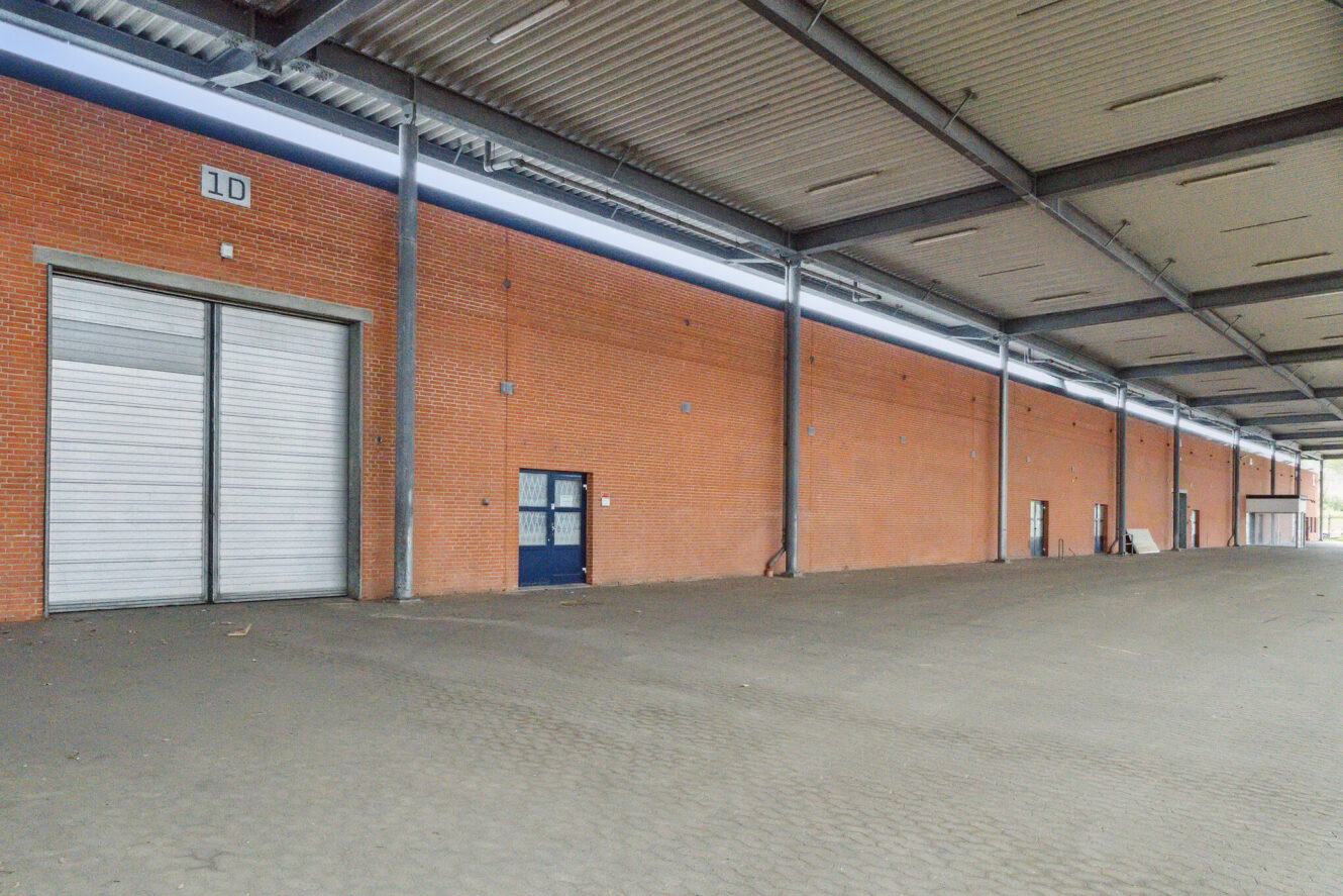 Stort, tomt industrielt læsserampeområde med en murstensvæg, flere lukkede rulleporte og et bredt, beskyttet udhæng.