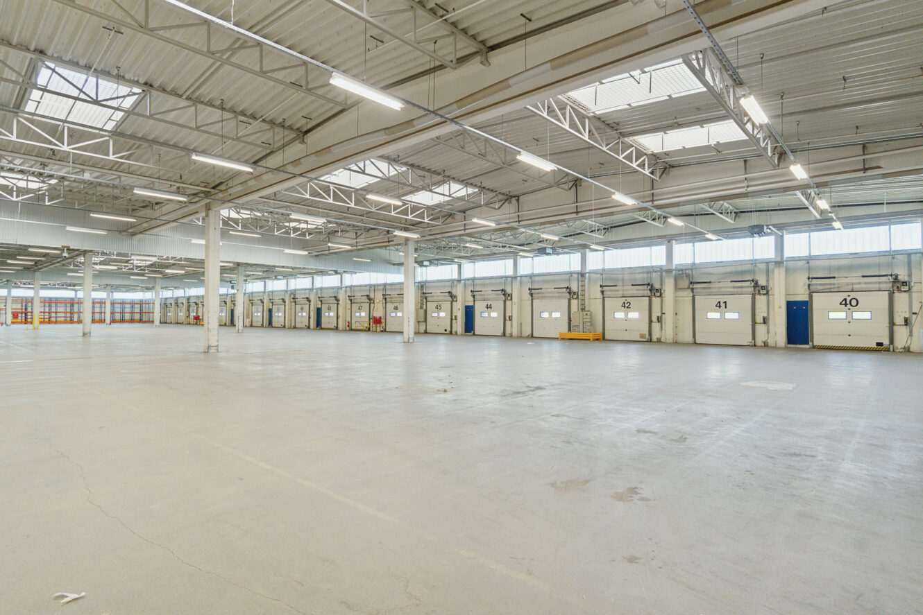 Rummelig, tom lagerbygning med højt til loftet, ovenlys og en række læsseramper langs den ene væg.