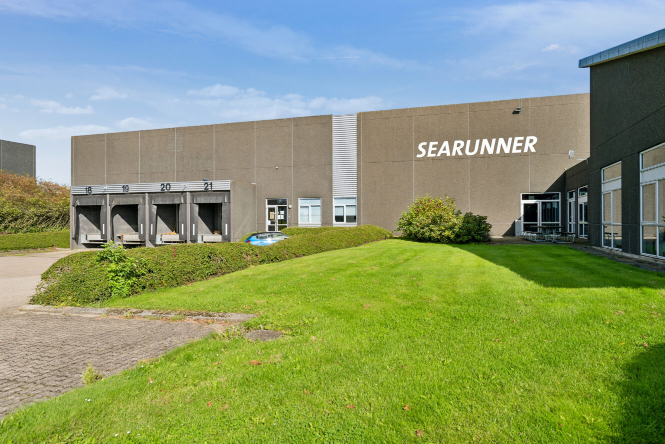 En stor industribygning med ordet SEARUNNER på facaden, med læsseramper og et græsareal foran.