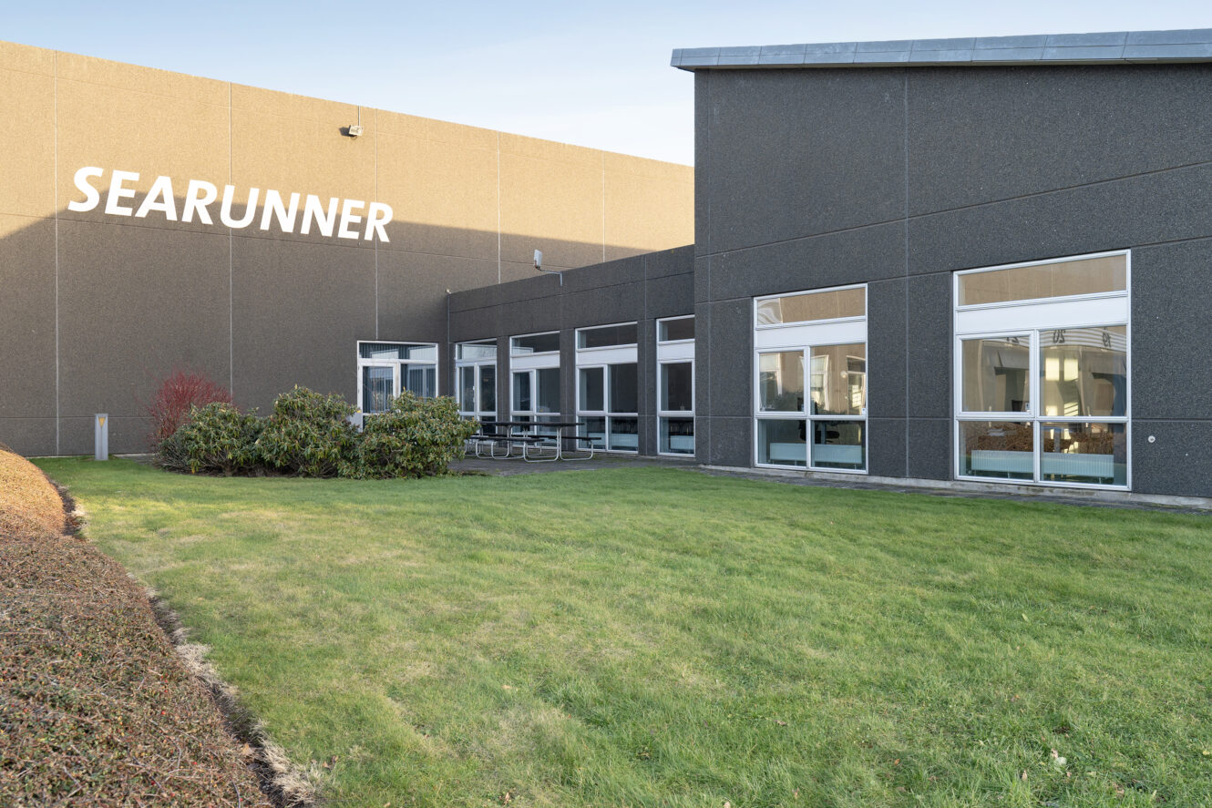 En moderne industribygning med navnet SEARUNNER med store vinduer og en velholdt græsklædt gårdhave foran.