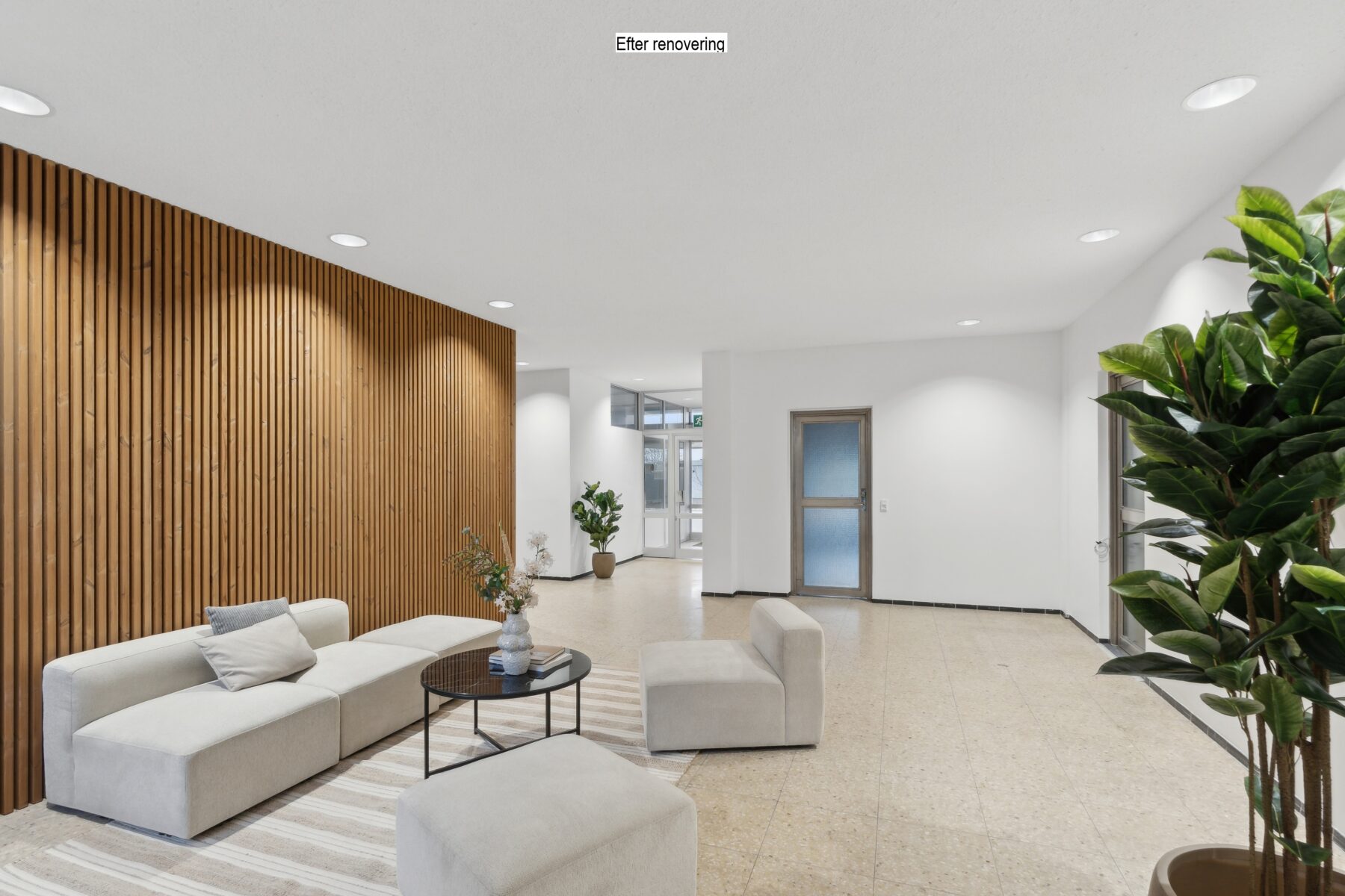 Moderne lobby med lyse møbler, et rundt sofabord, en væg med trælameller, potteplanter og naturligt lys fra store vinduer. På skiltet står der Efter renovering.