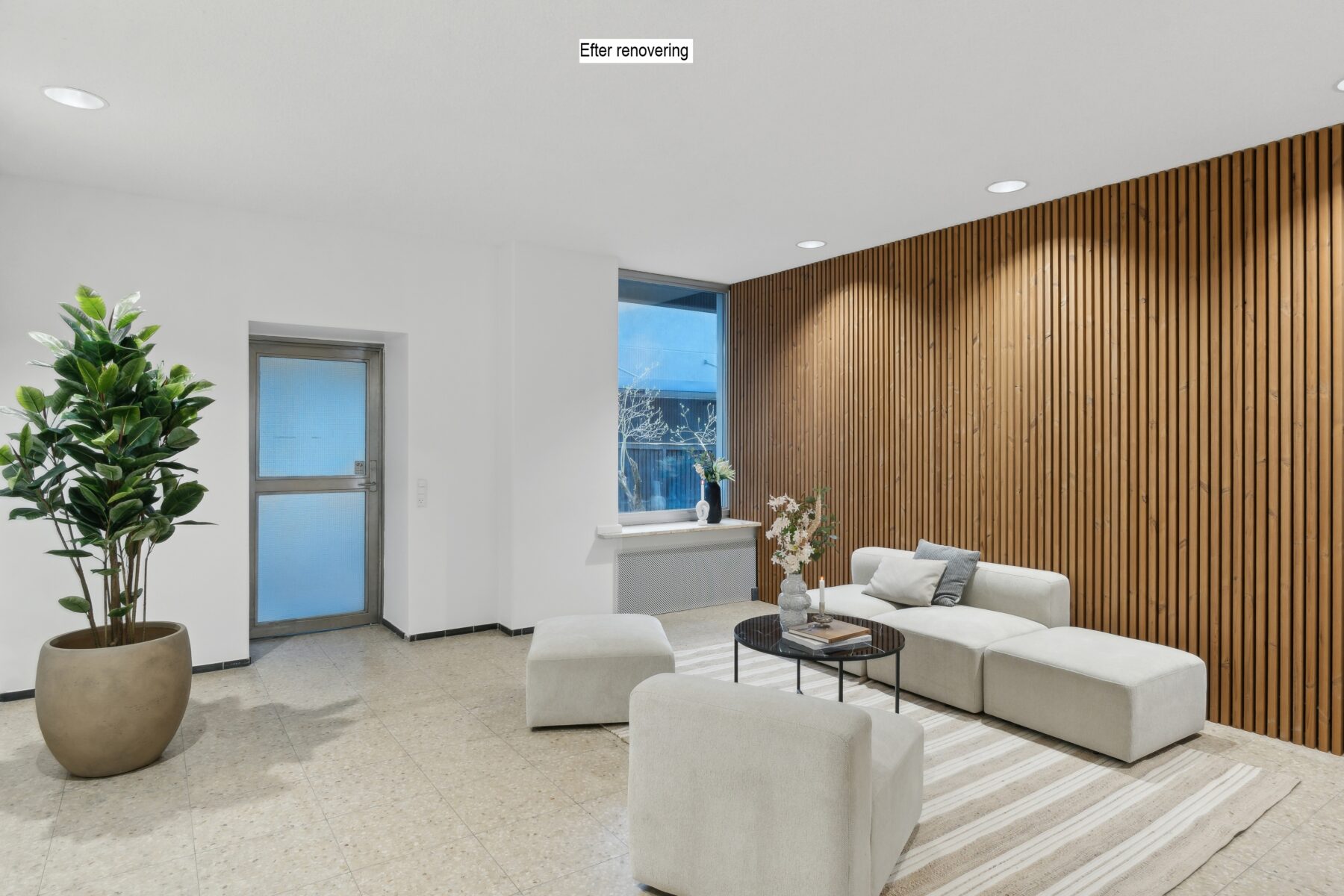 Moderne stue med en stor potteplante, hvid sektionssofa, rundt sofabord, stribet tæppe og accentvæg med træpaneler. På skiltet over billedet står der After renovating.