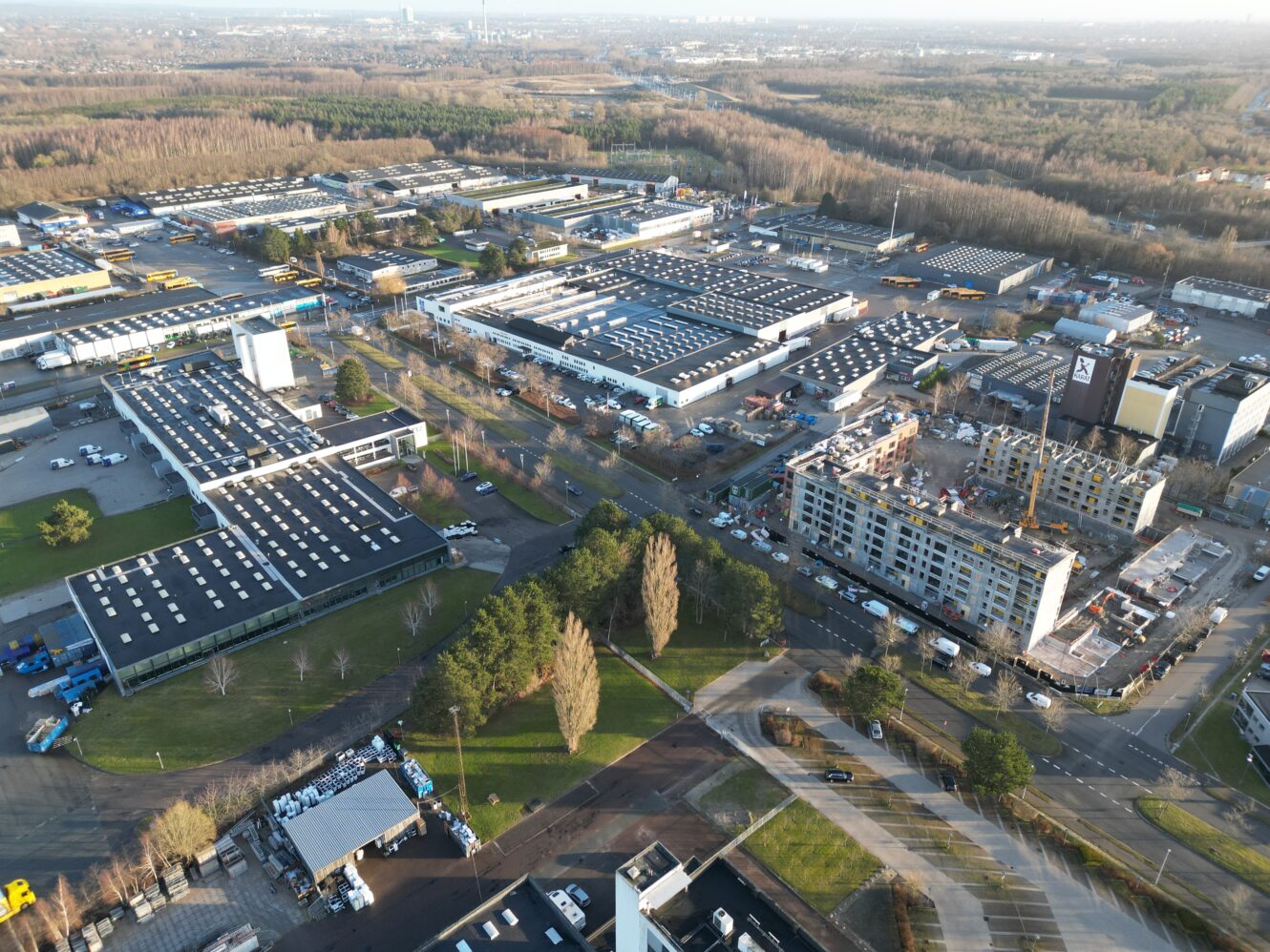 Luftfoto af et industriområde med flere store lagerbygninger, kontorbygninger, byggepladser, træer og omkringliggende veje.