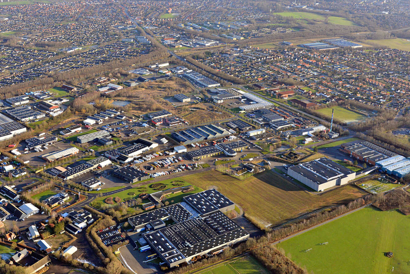 Luftfoto af et industriområde med lagerbygninger og fabrikker, omgivet af boligkvarterer og grønne marker.