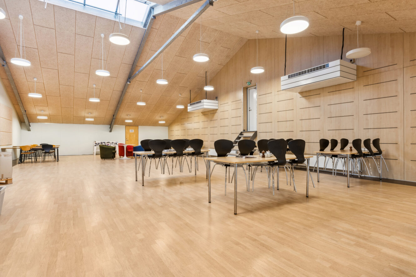 Et rummeligt, moderne lokale med trægulve, stablede stole på borde, ovenlys og store vinduer i loftet.