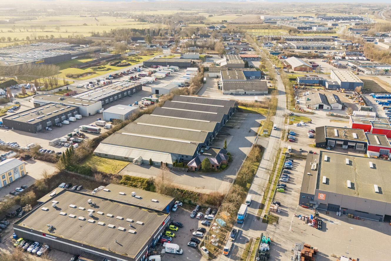 Luftfoto af et industriområde med store lagerbygninger, fyldte parkeringspladser og veje, der løber gennem komplekset, på en klar dag.