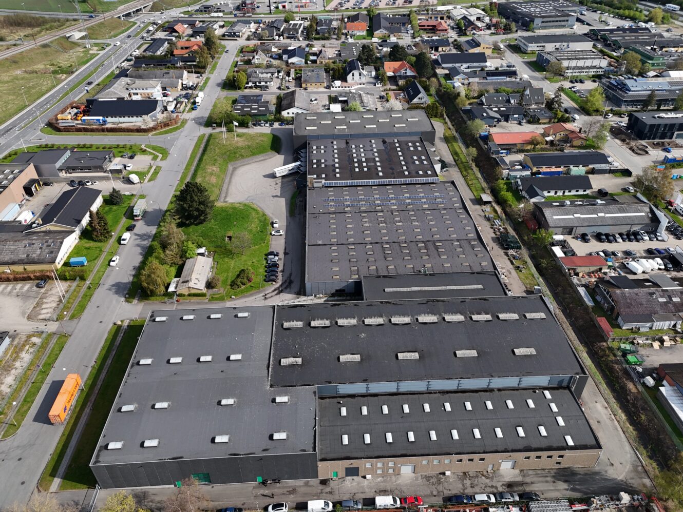 Luftfoto af et industrikompleks med store lagerbygninger omgivet af veje og boligområder.