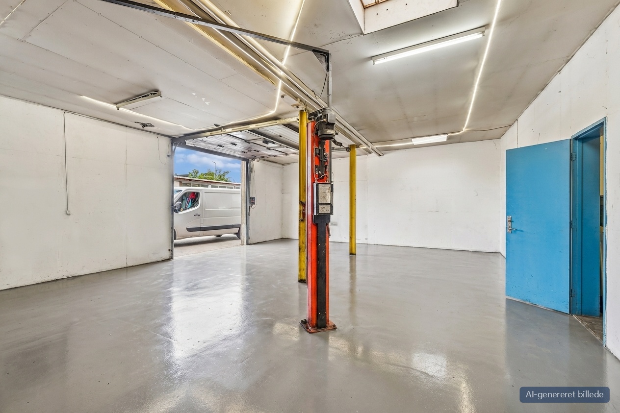 Tomt autoværksted med en lift i midten, poleret betongulv, åben hoveddør, blå sidedør og en hvid varevogn parkeret udenfor.