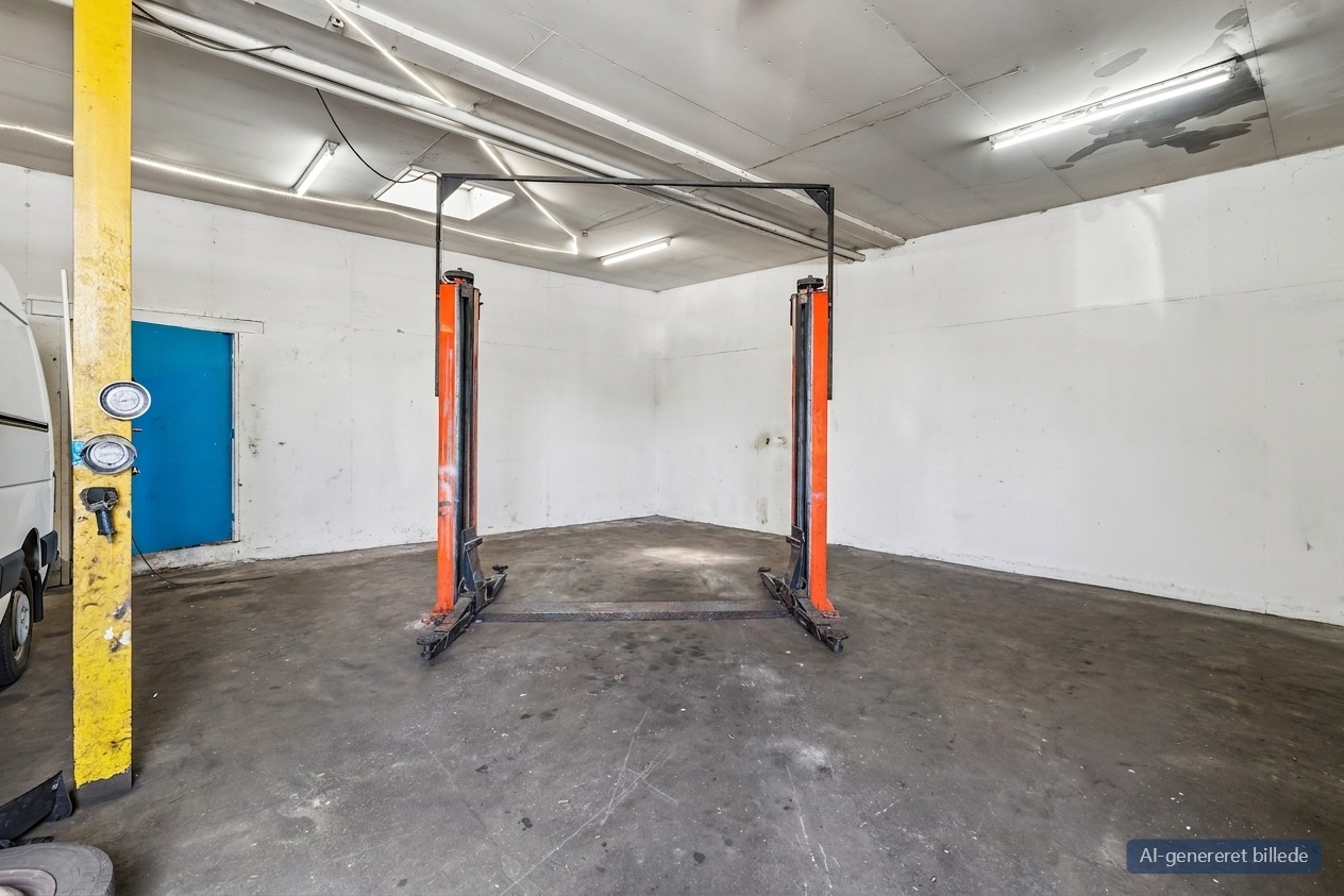 En tom autolift står i midten af en bar garage med betongulv, hvide vægge, lysstofrør og en blå dør til venstre.