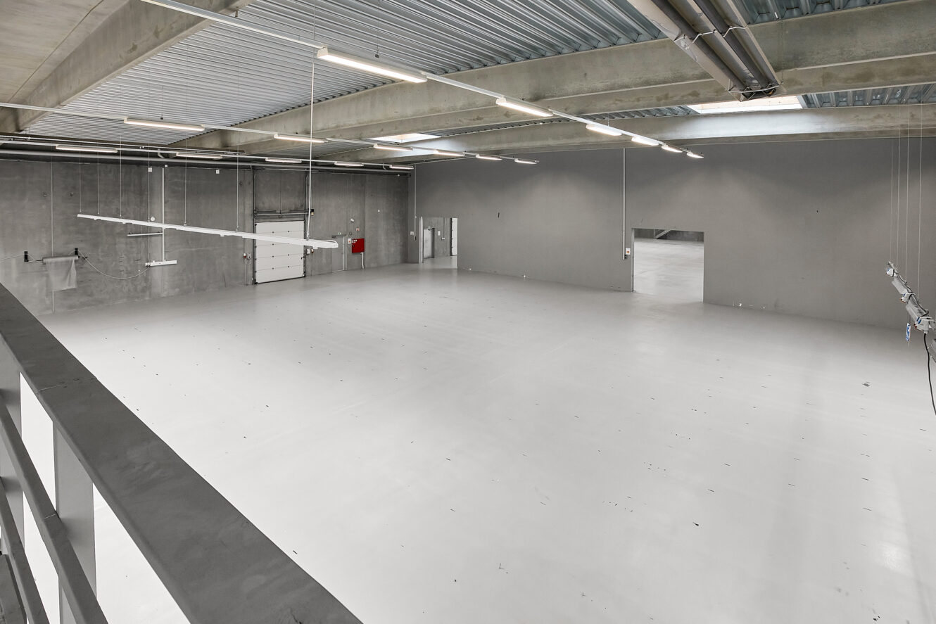 Tomt industrilager med betonvægge, højt til loftet, lysstofrør og en stor garageport på den ene side.