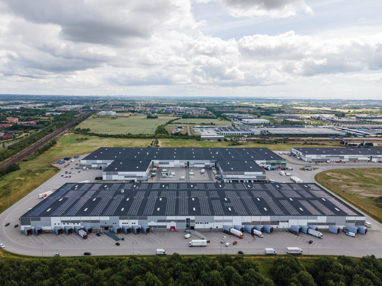 En stor lagerbygning med mange lastbiler parkeret på en parkeringsplads.
