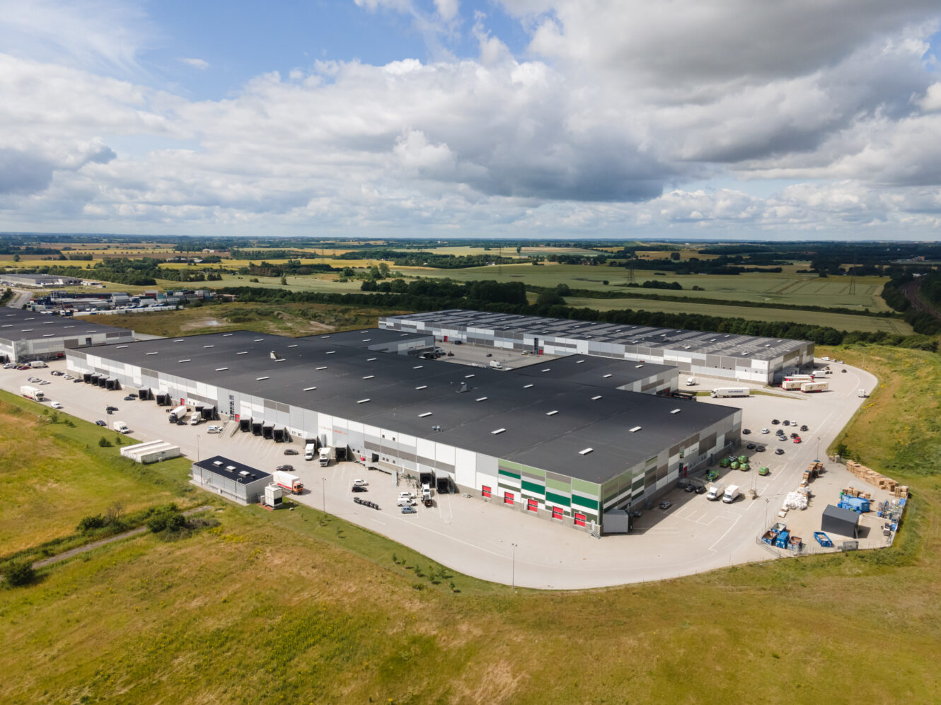 En stor lagerbygning med mange biler parkeret på en parkeringsplads.