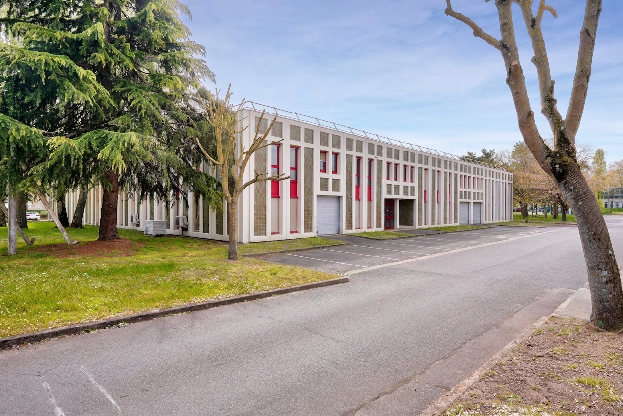 Un immeuble de bureaux moderne de forme rectangulaire, orné de rayures verticales blanches et de fenêtres aux accents rouges, se dresse au milieu des arbres, à côté d'un parking vide, sous un ciel dégagé.