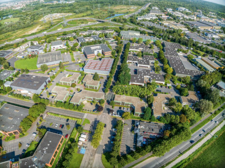 Vue aérienne d'un parc d'activités comprenant plusieurs immeubles de bureaux, des parkings et des espaces verts entourés de routes et d'autoroutes.