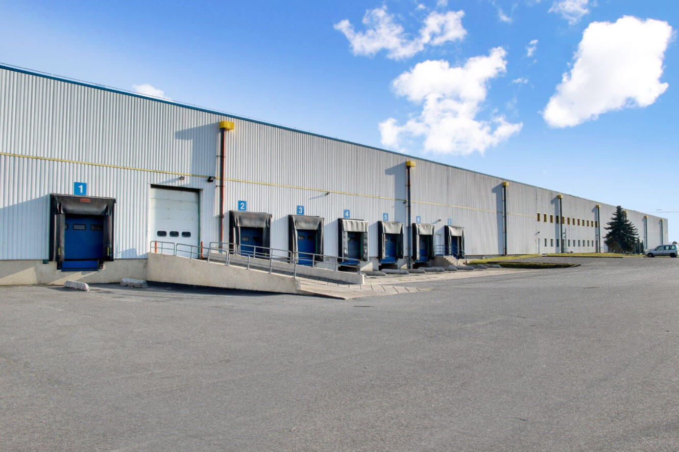 Un grand entrepôt avec plusieurs quais de chargement, tous numérotés et équipés d'abris de quai, sous un ciel partiellement nuageux.