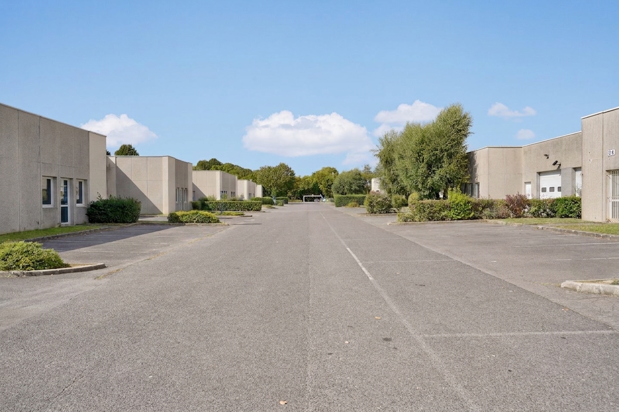 Vaste espace pavé situé entre deux rangées de bâtiments commerciaux bas au toit plat, avec un aménagement paysager minimaliste et un ciel dégagé et ensoleillé au-dessus.