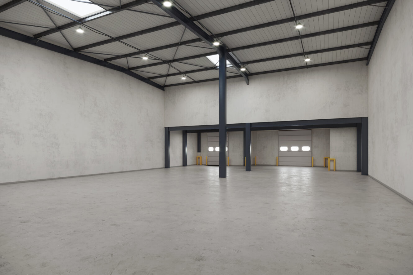 Entrepôt industriel vide avec hauts plafonds, sol en béton, murs blancs, poutres apparentes, éclairage zénithal, deux quais de chargement avec portes fermées et bornes de sécurité.