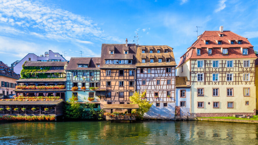 Rangée de maisons traditionnelles à colombages aux façades colorées se reflétant dans un canal sous un ciel bleu à Strasbourg, France.