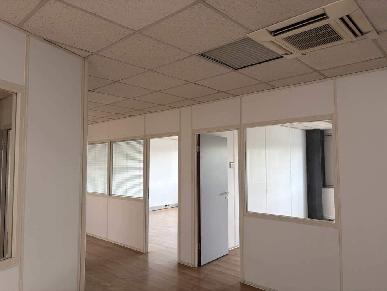 Espace de bureaux vide, avec des murs blancs, des cloisons vitrées, du parquet clair, des portes ouvertes et des pièces non meublées.
